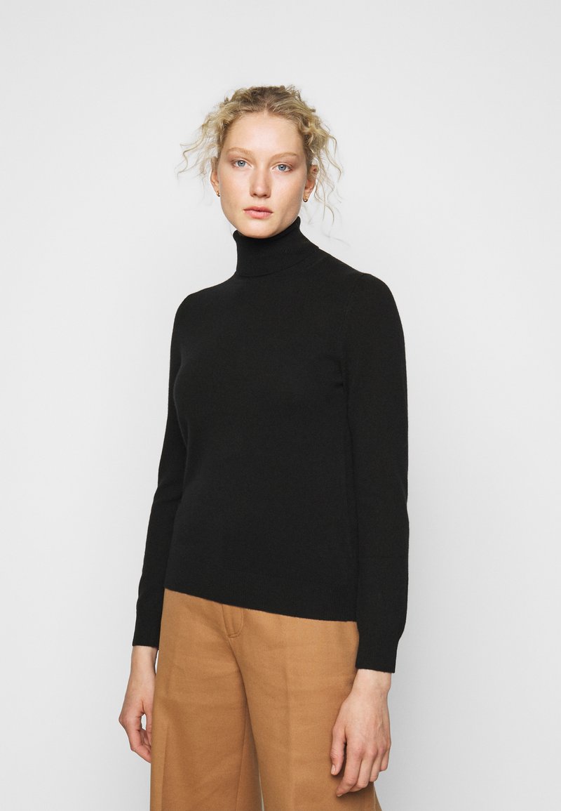 Svart høyhalset genser laget av et mykt strikket materiale. Stram design med lange ermer og ribbestrikket kant, kombinert med beige bukser.