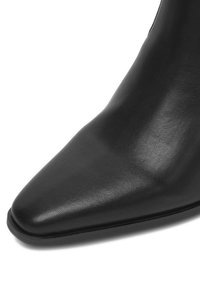 Zbliżenie czarnego skórzanego buta na szpilce z gładką fakturą i niską podeszwą, na białym tle.