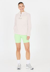 Lätt, ljusrosa zip-jacka med huva, kombinerad med klara gröna shorts. Modellen har på sig grå träningsskor och vita strumpor.