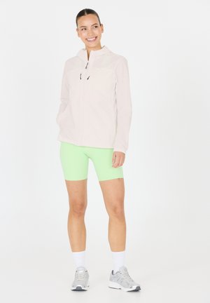 Lightweight, pale pink zip-up jacket with a hood, paired with bright green shorts. Model wearing gray athletic shoes and white socks.