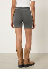 Sive ribane kratke hlače z visokim pasom, v kombinaciji z rjavimi usnjenimi škornji do kolen, ki imajo zaponko in debele črne podplate.