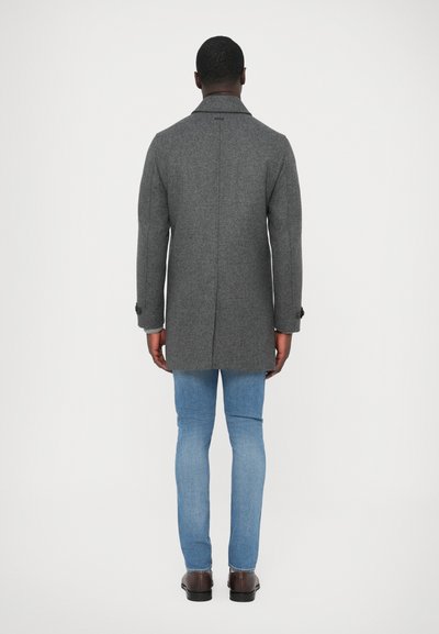 Γκρι μάλλινο παλτό με κομψό σχεδιασμό, μανσέτες με κουμπιά και ίσια γραμμή. Φοριέται πάνω από ανοιχτό μπλε τζιν και καφέ παπούτσια.