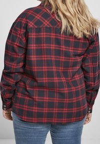 Röd och svart rutigt flanellskjorta med knäppning vid ärmslut, avslappnad passform och spetsig krage. Mjuk textur med ett rutig mönster.