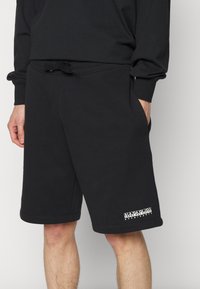 Shorts de sport noirs en tissu doux avec une taille élastique et un cordon de serrage, des poches latérales et un logo blanc sur l'ourlet.