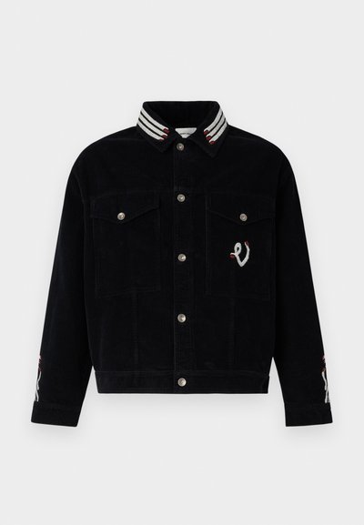 Juodasis kordūrojo švarkas su dryžuotu apykakle. Pridėtos metalinės sagos, dvi krūtinės kišenės ir siuvinėti akcentai ant rankovių.