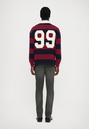 Navy and burgundy striped rugby shirt with white number "99" on back; paired with gray jeans and black shoes, viewed from the rear.