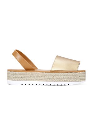 Sandalias de plataforma con tiras al tobillo en dorado y beige, con suela texturizada de yute, base de goma blanca y acabado metálico suave en la parte superior.