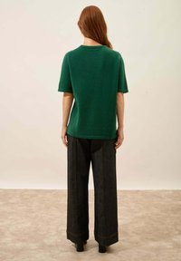 Zielona, krótkosourwana, dzianinowa bluzka w połączeniu z szerokimi ciemnoniebieskimi spodniami dżinsowymi z pomarańczowymi przeszyciami i wyraźną sylwetką. Czarne obuwie.