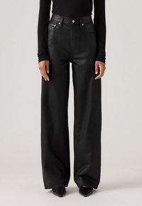 Zwarte wijde jeans van denim, met een hoge taille, sluiting met een knop aan de voorkant en een minimalistisch design, gecombineerd met puntige schoenen.