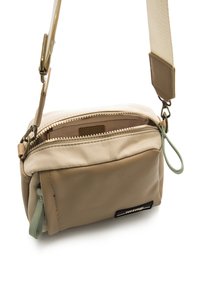 Bolso bandolera beige hecho de cuero suave y tela, con cierre superior con cremallera, texturas variadas y una pestaña de tirador en color verde.