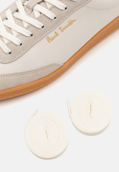 Valge nahast tenniseking, millel on beežist sametist detailid, tasased valged paelad ja pruun kummipohja. Kaasas on kaks täiendavat valge paela rulli.