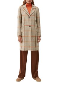 Abrigo de lana beige con patrón de cuadros naranjas, cierre de botones, cuello con muesca y dos bolsillos laterales, llevado sobre un suéter de cuello alto naranja brillante y pantalones marrones.