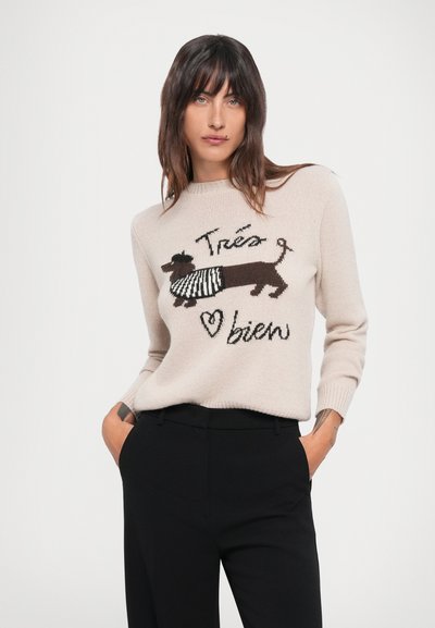 Beige knitted sweater featuring a brown dachshund illustration wearing a striped scarf, with the text "Trés bien" in black. Paired with black pants.
