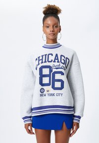 Szary, oversize'owy sweatshirt z niebieskim i żółtym graficznym wzorem z napisem "CHICAGO 86" oraz "NEW YORK CITY". Żebrowany kołnierz i mankiety, estrzowane detale.