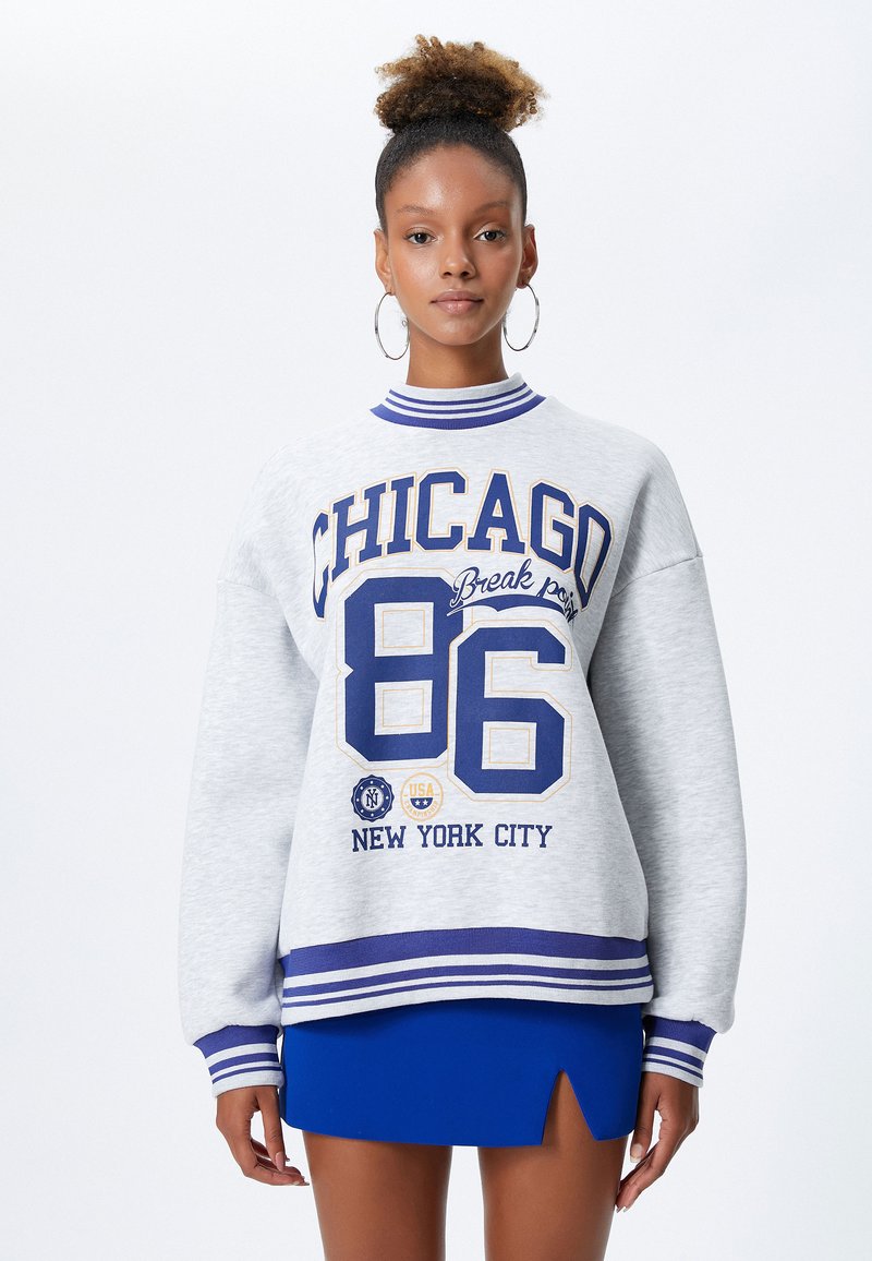 Szary, oversize'owy sweatshirt z niebieskim i żółtym graficznym wzorem z napisem "CHICAGO 86" oraz "NEW YORK CITY". Żebrowany kołnierz i mankiety, estrzowane detale.