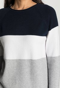 Maglione a blocchi di colore con sezioni blu navy, bianche e grigie; texture morbida; scollatura a girocollo; maniche raglan.