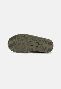 Suela de zapato de goma en verde oliva con patrón de copo de nieve y ranuras horizontales para tracción. Presenta un corte rectangular y una marca en relieve.