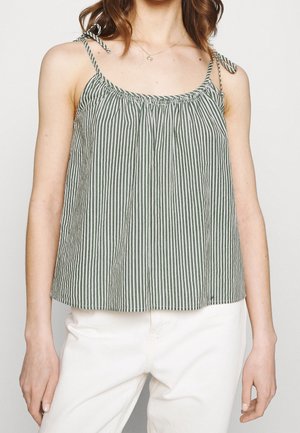Nainen, jolla on harmaa ja valkoinen pystysuora raidallinen hihaton toppi, jossa on solmittavat hihnat, ja valkoiset housut, yläosa leikattu kaulan ja lantiolta.