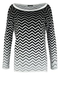 Pull en chevrons noir et blanc avec des manches longues et un large col, affichant une texture en tricot doux qui dégrade du noir au blanc.