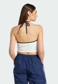 Vit halterneck crop top med marinblå kant, med en knuten baksida. Matchad med mörkblå byxor med elastisk midja. Slät tyg, avslappnad stil.
