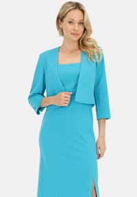 Turkusowa sukienka z rękawami do trzech czwartych, z dopasowanym krojem i bocznym rozcięciem. Gładka tekstura, kwadratowy dekolt oraz skrócona marynarka.