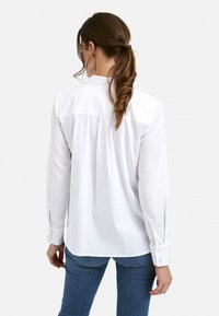 White long-sleeve shirt with a button-down collar, featuring a back pleat and cuff buttons. The fabric appears smooth and lightweight.