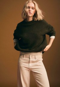 Übergroßer, dunkelgrüner Strickpullover mit geripptem Ausschnitt und Saum, kombiniert mit hellrosa hochtaillierten Jeans. Einfarbig, weiche Textur.