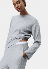 Light gray ribbed knit sweater with long sleeves, crew neck, and a relaxed fit, paired with matching pants featuring side pockets.