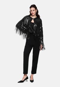 Black sequin fringed cape with a round neckline, worn over a satin top and paired with tailored black trousers and pointed black heels.
