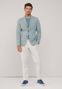 Blazer a quadri blu chiaro con due bottoni, abbinato a una t-shirt turchese, pantaloni bianchi e sneakers blu. Texture liscia in tutto l'abbigliamento.