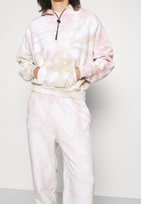 Hoodie tie-dye rosa e crema con cappuccio con cordino, tasca a marsupio e pantaloni coordinati. Tessuto morbido con vestibilità comoda.