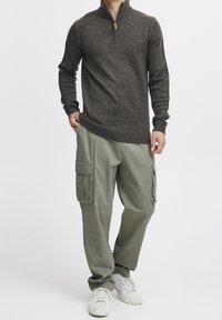 Ciemnoszara bluza zapinana na zamek z prążkowanymi mankietami i dolnym brzegiem, w połączeniu z jasnooliwkowymi spodniami cargo z bocznymi kieszeniami. Białe sneakersy dopełniają stylizację.