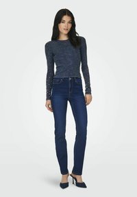 Jeans aderenti blu scuro in denim, abbinati a un top lungo navy con dettagli in perle sulle maniche.