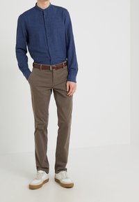 Granatowa koszula na guziki z długim rękawem, brązowy pasek, jasnobrązowe spodnie i białe trampki z beżowymi akcentami, stojące na jednolitym tle.