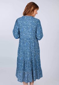 Blaues Blumenkleid mit Puffärmeln, gestuftem Saum und einem Muster aus weißen und grünen Blumen auf einem strukturierten Hintergrund.