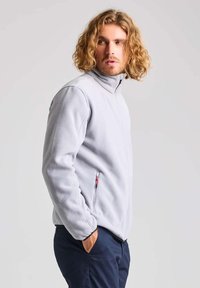 Giacca in fleece grigio chiaro con colletto alto, zip completa e tasche laterali con dettagli rossi. Texture morbida e vestibilità casual.