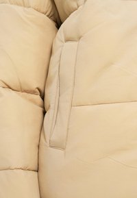 Ύφασμα μπουφάν μπεζ, με ραμμένα τμήματα και πλαϊνή θήκη. Απαλή υφή με ραφές και λεία επιφάνεια.