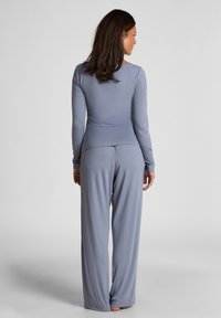 Lichtgrijs langemouwtop en wijde broek gemaakt van zachte, gladde stof. Relaxte pasvorm, minimale naden en subtiele ontwerpelementen.