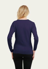 Chemise à manches longues, bleu marine, en tissu doux, avec un col rond et une conception ajustée, portée avec un pantalon noir.