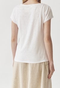 Weißes, kurzärmliges T-Shirt mit rundem Ausschnitt. Weiche Textur, leichter Glanz und lässige Passform, kombiniert mit einem beigen, leinenähnlichen Rock.