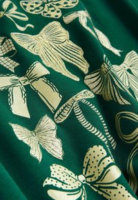 Zielony materiał z różnymi złotymi metalicznymi kokardkami w różnych kształtach, rozmiarach i wzorach, w tym w kropeczki i plisowane.