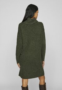 Abito maglione di grandi dimensioni, di colore verde scuro, con colletto alto, maniche lunghe e orlo a coste. Texture morbida con finitura lavorata a maglia e spacchi laterali.