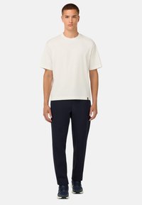 Vit bomull t-shirt med korta ärmar, matchat med mörk marinblå byxor. Platt fåll, slät textur och subtil logotypdetalj vid fållen.