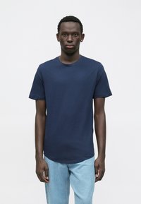 Námořnicky modré bavlněné tričko s krátkými rukávy, kulatým výstřihem a volným střihem. Nošeno s světle modrými džínami.