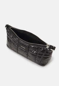 Pochette matelassée noire avec fermeture éclair, présentant un extérieur élégant, une quincaillerie argentée et une étiquette de marque sur le devant.