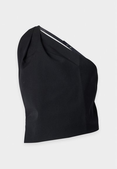 Crop top asymétrique noir à une épaule avec une fine bretelle réglable sur le côté gauche, présenté sur un fond clair.