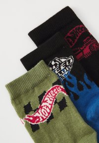 Tre paia di calzini di cotone: neri con grafica rossa, verdi con logo e motivo a scacchi, blu con design a fiamma. Colori e motivi diversi.