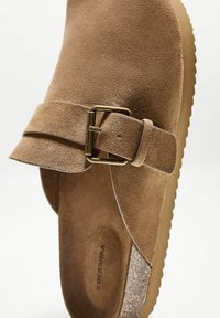 Rjava usnjena gležnjarica z odprtim zgornjim delom, širokim trakom in kovinsko zaponko. Debel podplat z teksturirano površino. Notranjost z mehko podlogo.