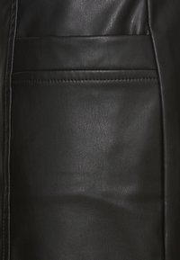 Musta nahkamateriaali, jossa on sileä pinta, koristeelliset ompeleet ja sivutasku. Muotoilu on yksinkertainen ja toimiva.