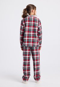Rode en groene geruite flanellen pyjama set met lange mouwen en losse broek met witte accenten en elastische tailleband.